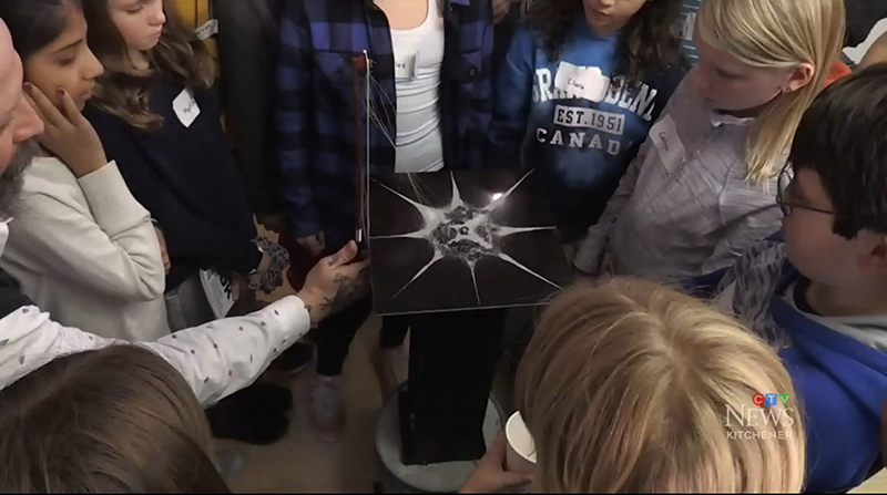 Students gathered around a pedestal for a demonstration of vibration frequency