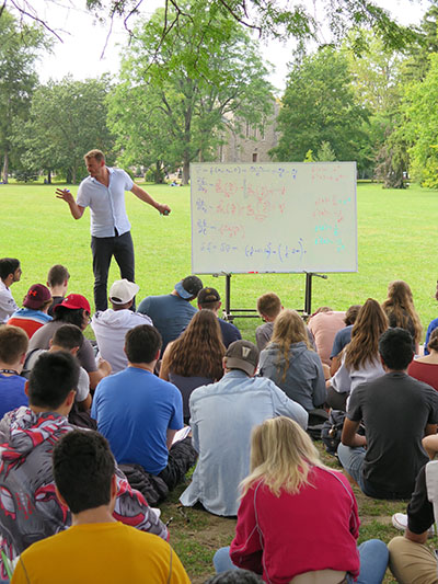 Dr. Dennis Muecher teaching outside to a group of students sitting on Johnston Green