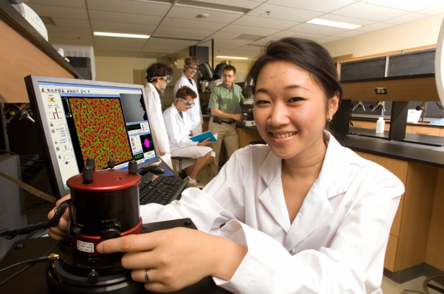 Student in foreground with microscope and computer monitor display of sample